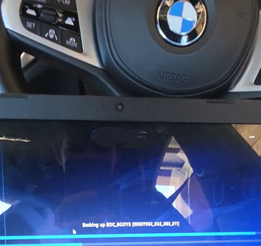 Laptop backing up a BMW body control module, with the steering wheel behind it